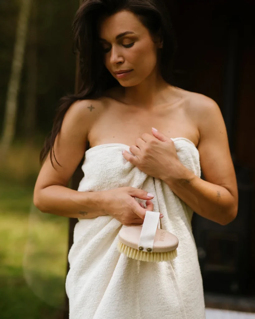 Kobieta w ręczniku lnianym frotte off white ze szczotką z naturalnym włosiem tampico w ręce.