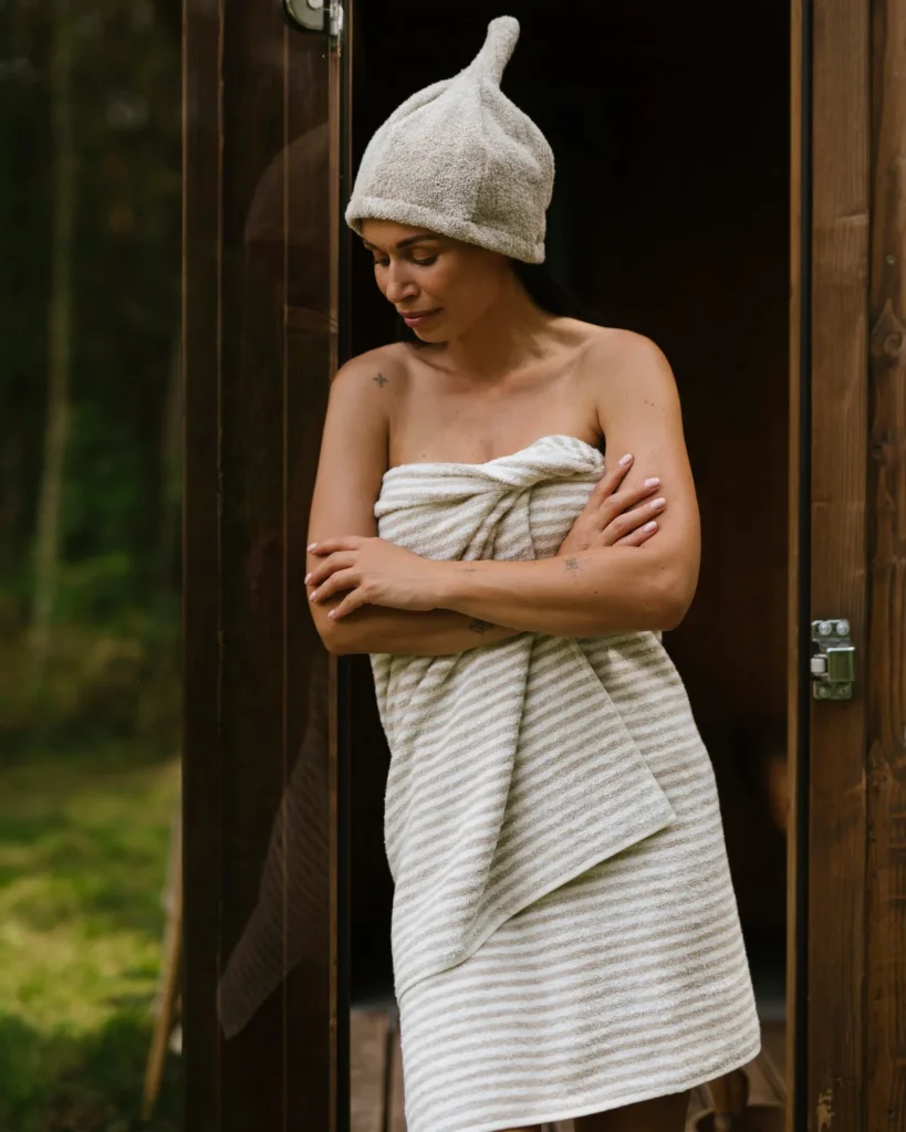 Kobieta w ręczniku w paski striped frotte len stoi przed sauną.