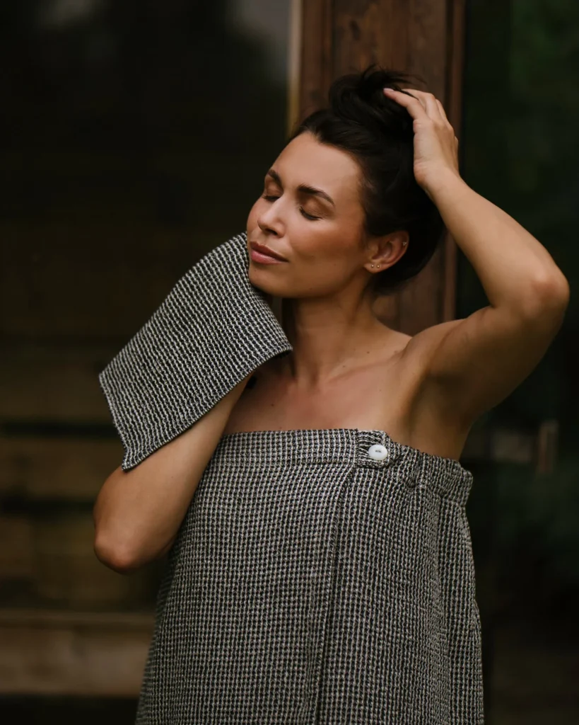 Kobieta wyciera twarz małym ręcznikiem do twarzy lnianym wafel natural black.