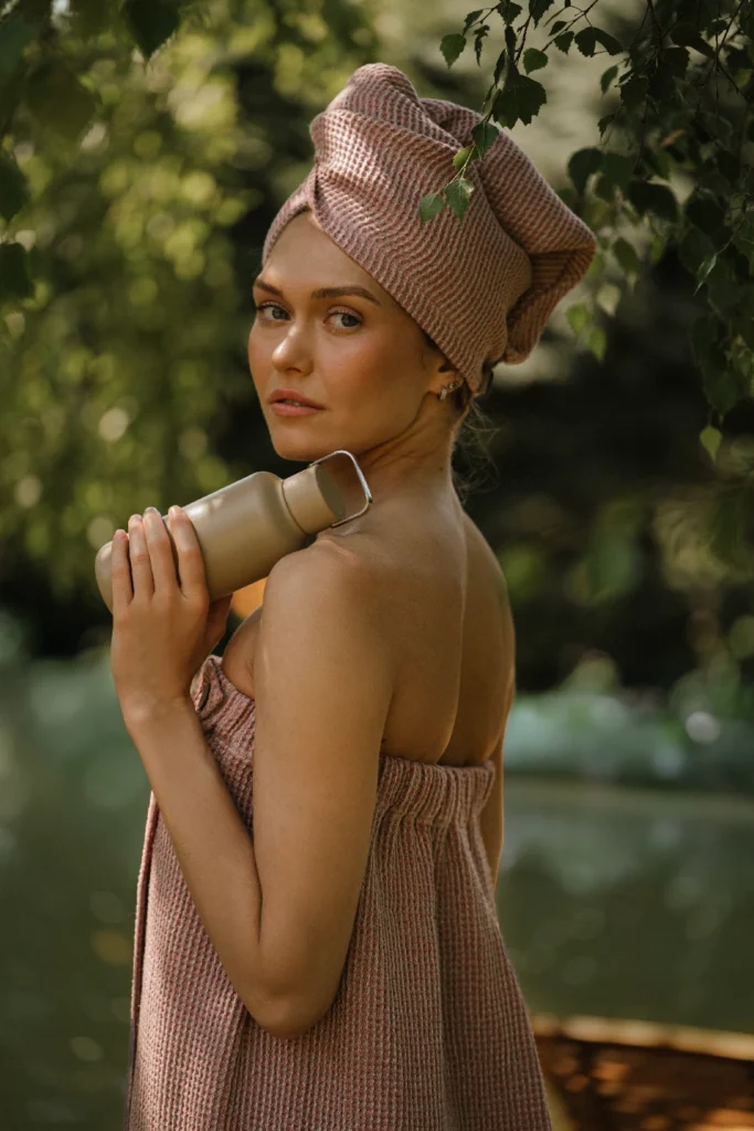 kobieta po saunowaniu ubrana w lniany turban do włosów, naturalne lniane pareo, trzymająca butelkę ze stali nierdzewnej