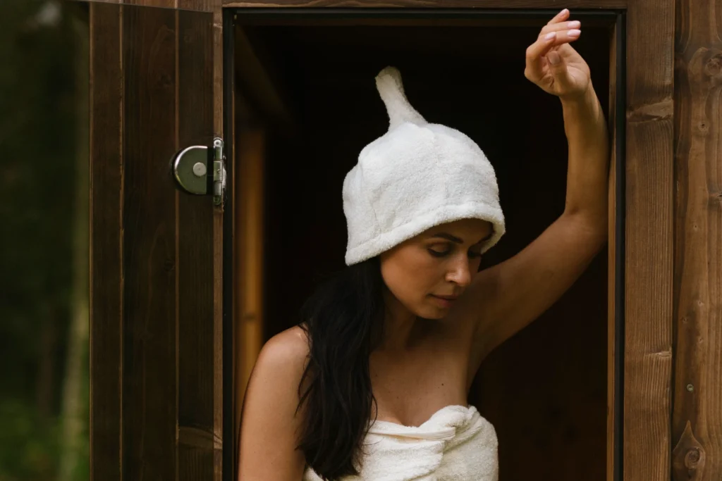 kobieta w trakcie saunowania ubrana w czapkę do sauny frotte i okryta ręcznikiem do sauny frotte